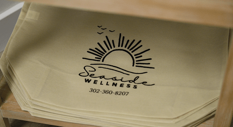 Seaside Wellness logo on stacked tote bags